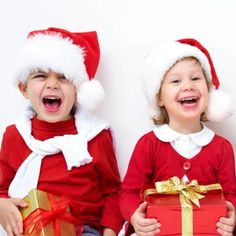 two young children wearing santa hats and holding presents