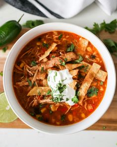 a white bowl filled with tortilla soup on top of a wooden cutting board