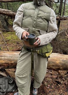 a man standing in the woods holding a coffee cup and wearing a protective gear outfit