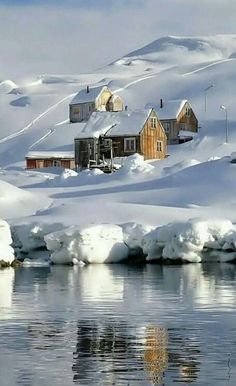 the snow covered mountains and houses are reflected in the still water at the edge of the lake