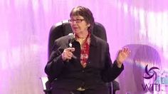 a woman sitting in a chair with her hands up and talking into a microphone on stage