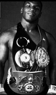 a man with a belt around his neck and some medals on his chest, standing in front of a black background