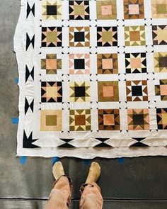 a person standing next to a quilt on top of a cement floor with their feet propped up