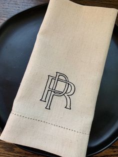 the monogrammed napkin is on top of a black plate with a white cloth