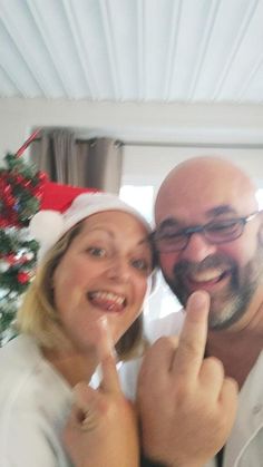 a man and woman posing for a photo in front of a christmas tree with their fingers up