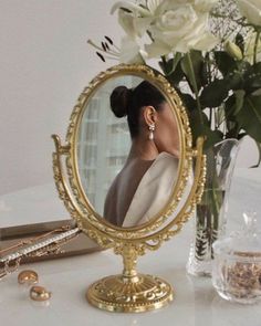 a woman's face is reflected in a gold vanity mirror next to jewelry and flowers