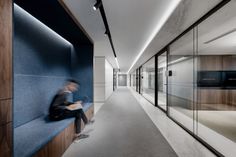 a man sitting on a bench in an office building with glass walls and floor to ceiling windows