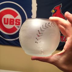 a person holding up a glass ball in front of a chicago cubs logo on the wall