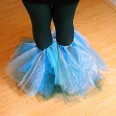 the legs of a person wearing blue tutuffs and black tights, standing on a wooden floor