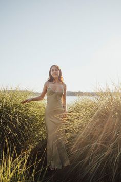 a woman in a long dress walking through tall grass with her arms out to the side