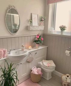 a white bathroom with pink accessories on the counter and toilet, sink, mirror and potted plant