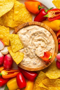 a wooden bowl filled with dip surrounded by chips and veggies