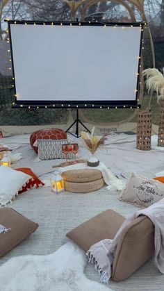 an outdoor movie screen surrounded by pillows, blankets and other decorative items on the ground