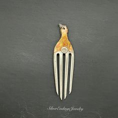 a metal comb with a bird on it's head hanging from the side, against a black background