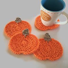 three crocheted pumpkin coasters sitting next to a coffee cup