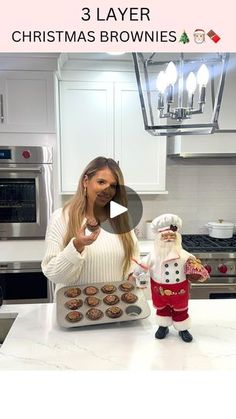 a woman standing in front of a kitchen counter holding a tray of cupcakes