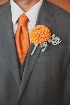 a man in a gray suit with an orange boutonniere on his lapel