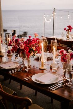 a table set for dinner with candles and flowers in vases on the table next to the ocean