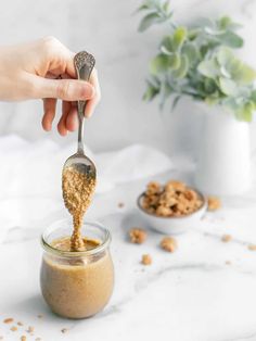 a person holding a spoon full of peanut butter and oatmeal mixture in a jar