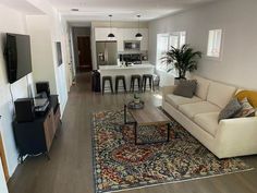 a living room filled with furniture and a flat screen tv mounted to the wall next to a kitchen