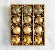 a wooden box filled with gold and silver christmas ornament ornaments on top of a white surface