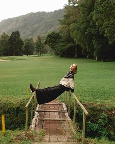 a woman laying on top of a wooden hand rail in a field next to trees