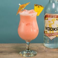 a pink cocktail with a pineapple garnish and a bottle of vodka next to it