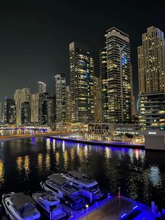 several boats are docked in the water near some buildings at night with bright lights on them