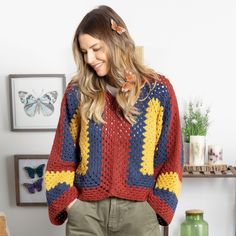 a woman standing in front of a wall wearing a multicolored crocheted sweater