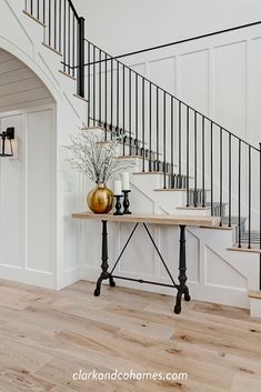 a vase with flowers sitting on top of a wooden table next to a stair case