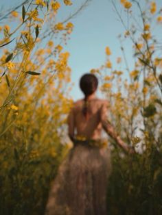 a woman is standing in the middle of a field with yellow flowers on her back