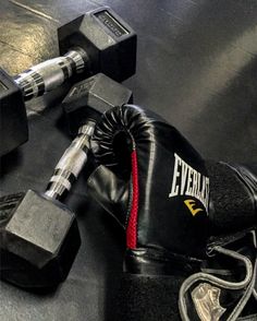 a pair of black boxing gloves sitting on top of a gym floor next to two dumbbells