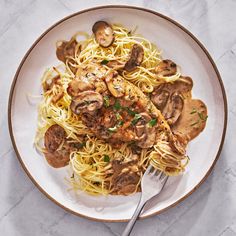 a white plate topped with pasta covered in mushroom sauce and chicken breast pieces next to a fork