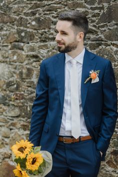 a man in a blue suit and white shirt holding a bouquet of sunflowers