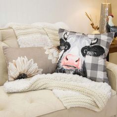 a cow pillow sitting on top of a couch next to a white chair and lamp