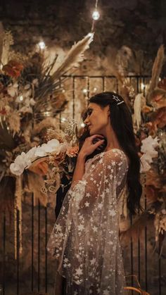 a woman standing in front of a wall with lots of flowers and feathers on it