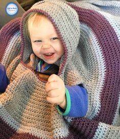 a little boy sitting in a car seat wrapped in a blanket and smiling at the camera