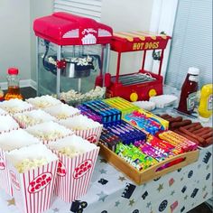 a table topped with popcorn buckets filled with cake and candy next to a hot dog stand