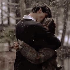 a man and woman hug in the rain while they are dressed in winter clothes,