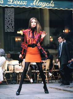 a woman in an orange dress and black jacket is standing on the street with her hands out