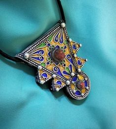 Ancient Berber talisman (herz) in sterling silver, enamelled in blue, green and yellow color. and decorated with a real coral cabochon. Height: 7 cm. Width: 5.5 cm. Leather: 54 cm. ++Material: sterling silver 925, real coral cabochon. ++Weight: 31.8 grams. ++ Origin: Morocco 1970s. Free worldwide shipping by DHL. I am always open to offers for one of my items, so please contact me if you would like to make an offer. Don't hesitate to contact me for any questions. All items advertised for sale ar Filigree Pendant Amulet Necklace, Traditional Handmade Heart Jewelry, Traditional Handmade Heart-shaped Jewelry, Traditional Heart Shaped Jewelry Gift, Traditional Heart-shaped Jewelry Gift, Unique Heart-shaped Festival Jewelry, Bohemian Engraved Jewelry As Gift, Bohemian Engraved Jewelry Gift, Bohemian Amber Jewelry With Large Pendant