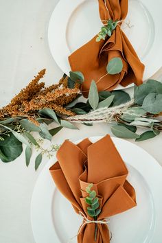 two white plates topped with napkins and greenery