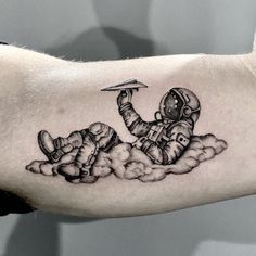 a man's arm with a black and white tattoo of an astronaut in the clouds