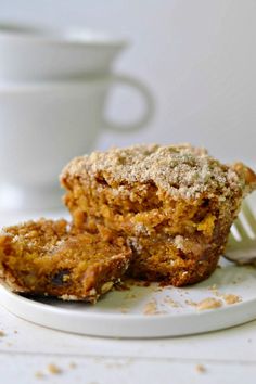 two muffins sitting on top of a white plate next to a cup and fork