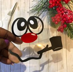 someone cutting out a face with scissors on top of a wooden table next to christmas decorations