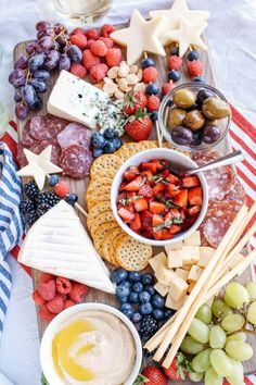 an assortment of cheeses, fruit and crackers on a platter with dip