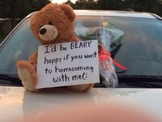 a teddy bear sitting on the hood of a car with a sign attached to it