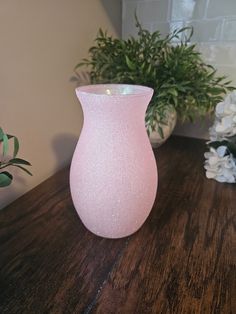 a pink vase sitting on top of a wooden table next to a potted plant