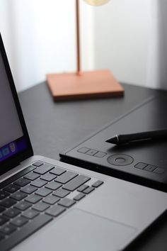 an open laptop computer sitting on top of a desk next to a pen and paper