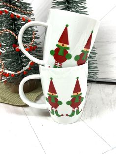 two coffee mugs decorated with santa hats and candy canes next to a christmas tree